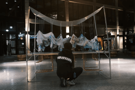 Student examining their suspended fabric and metal-frame installation exhibited at night