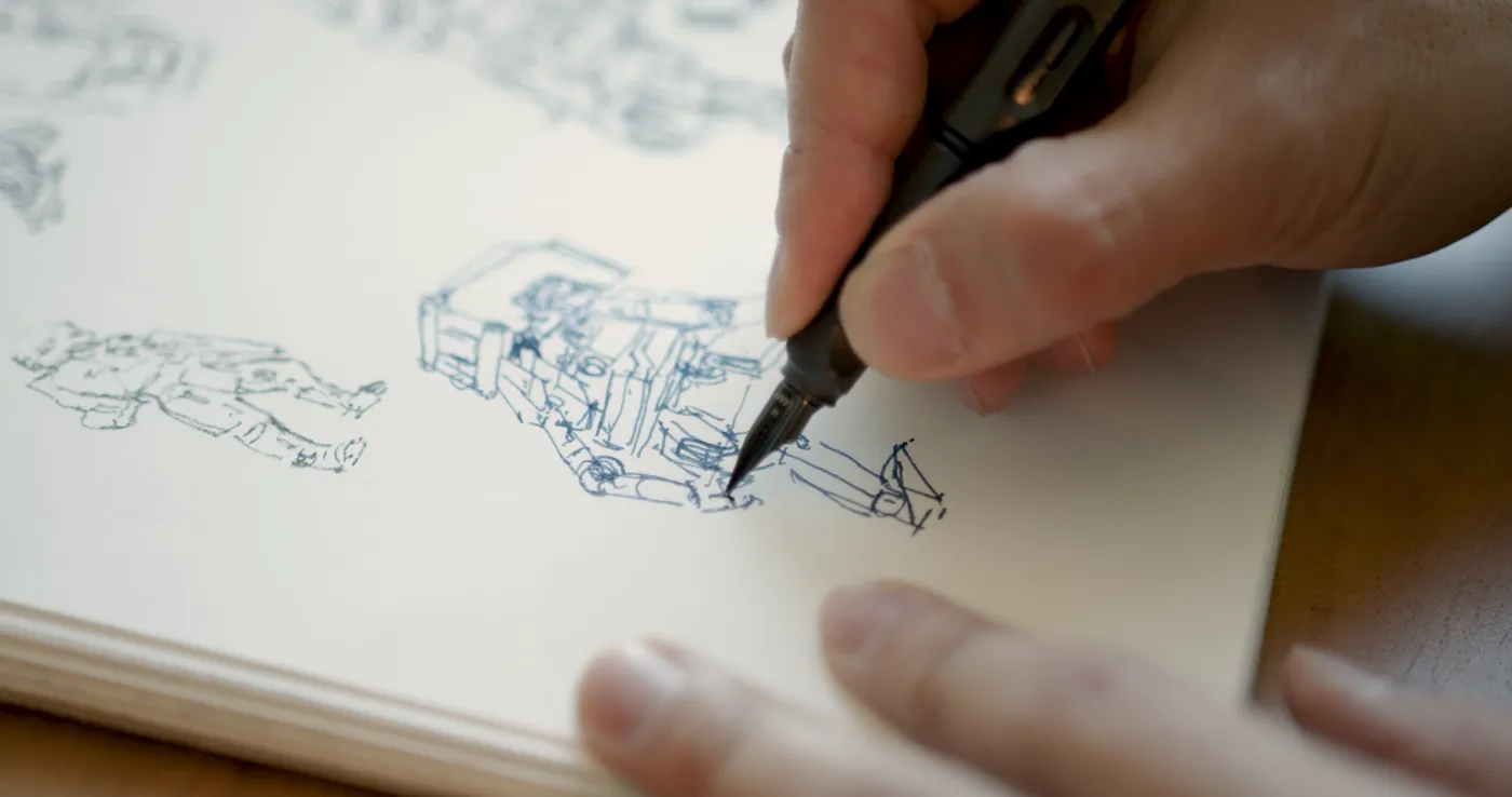 Close-up of a hand inking vehicle sketches in a sketchbook