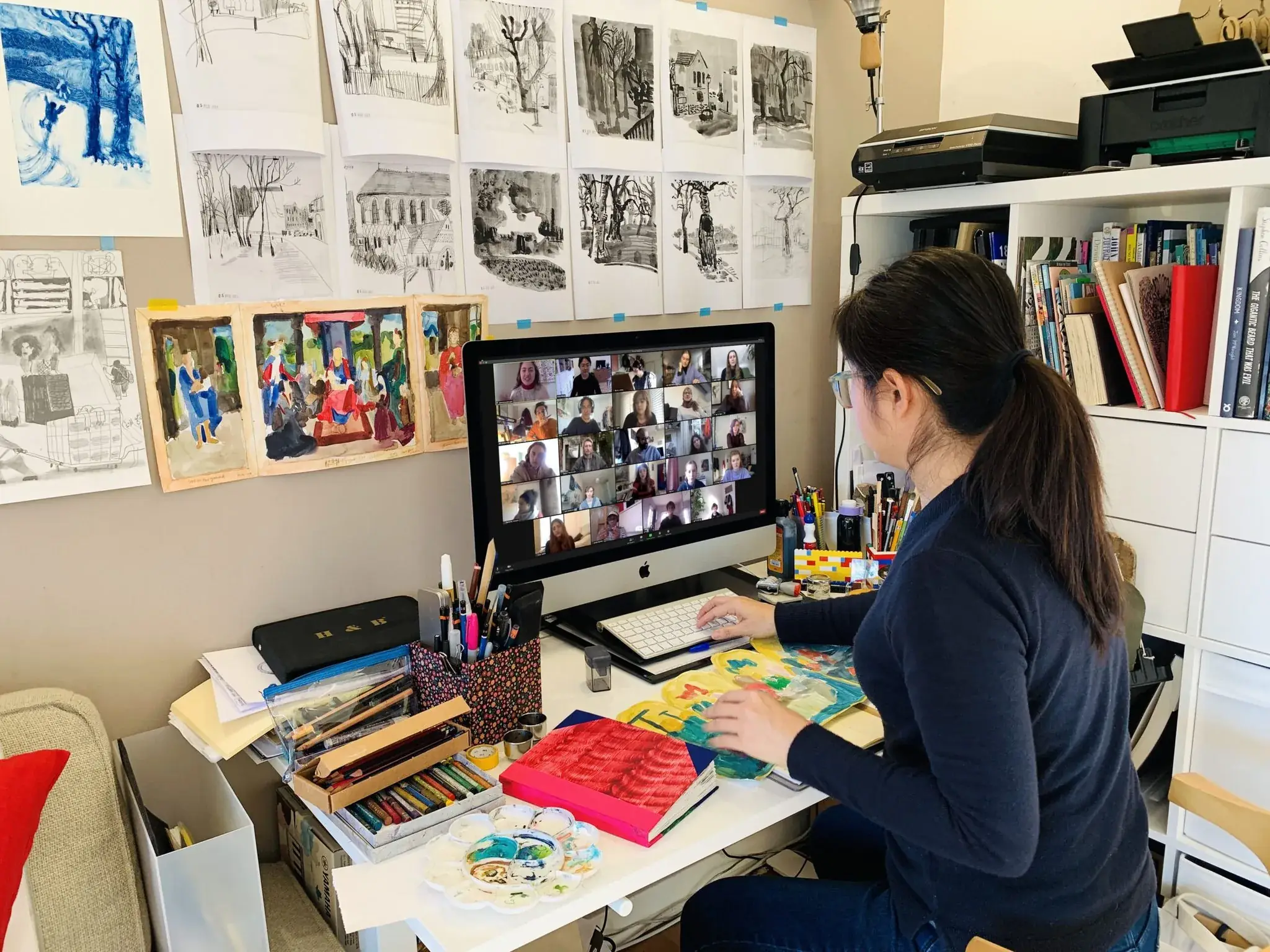 插画师坐在书桌前参加多人视频通话，四周墙上钉满了草图和水彩作品