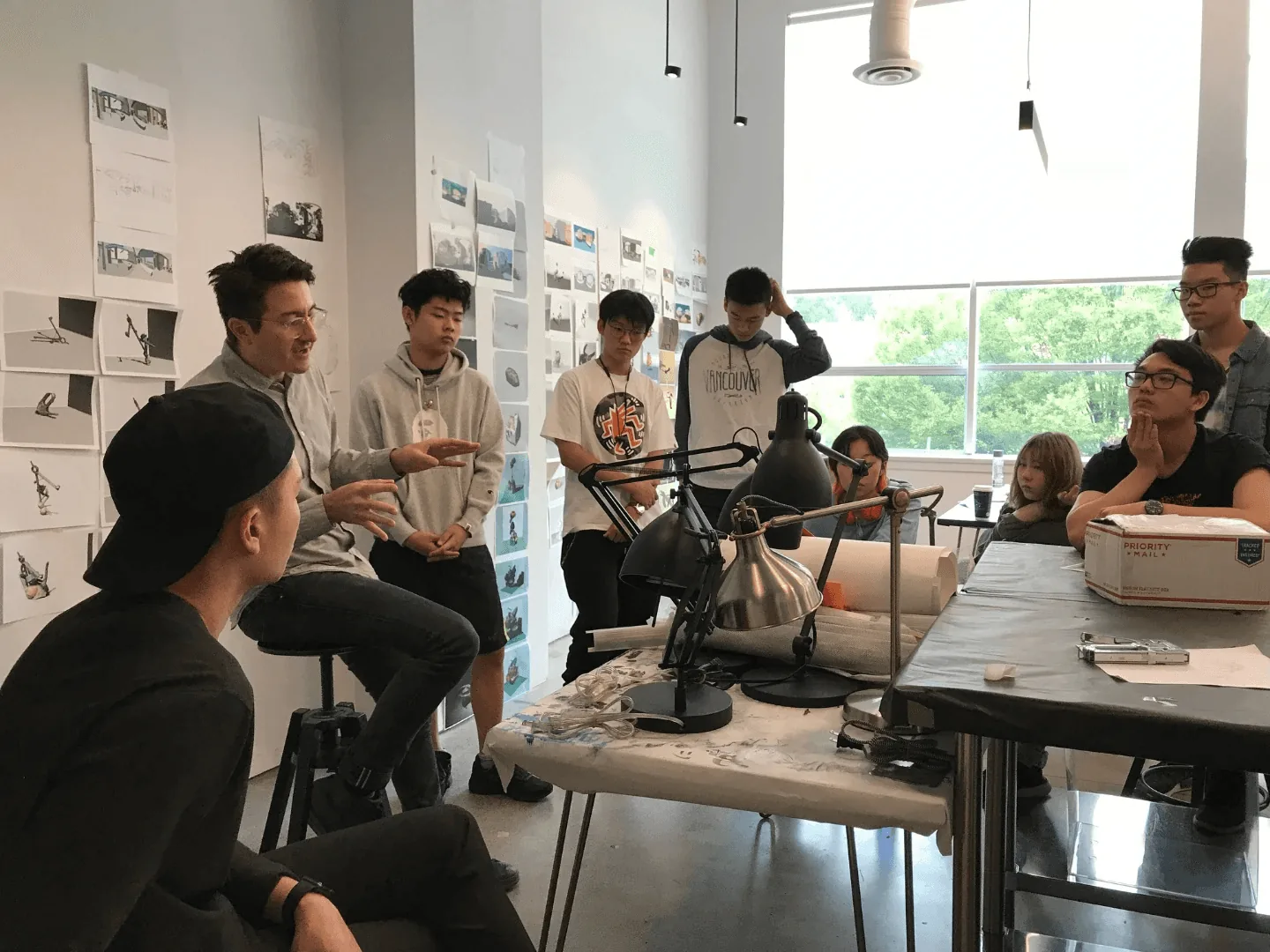 导师在贴满草图的工作室里，带领青少年学生进行小组作品评析