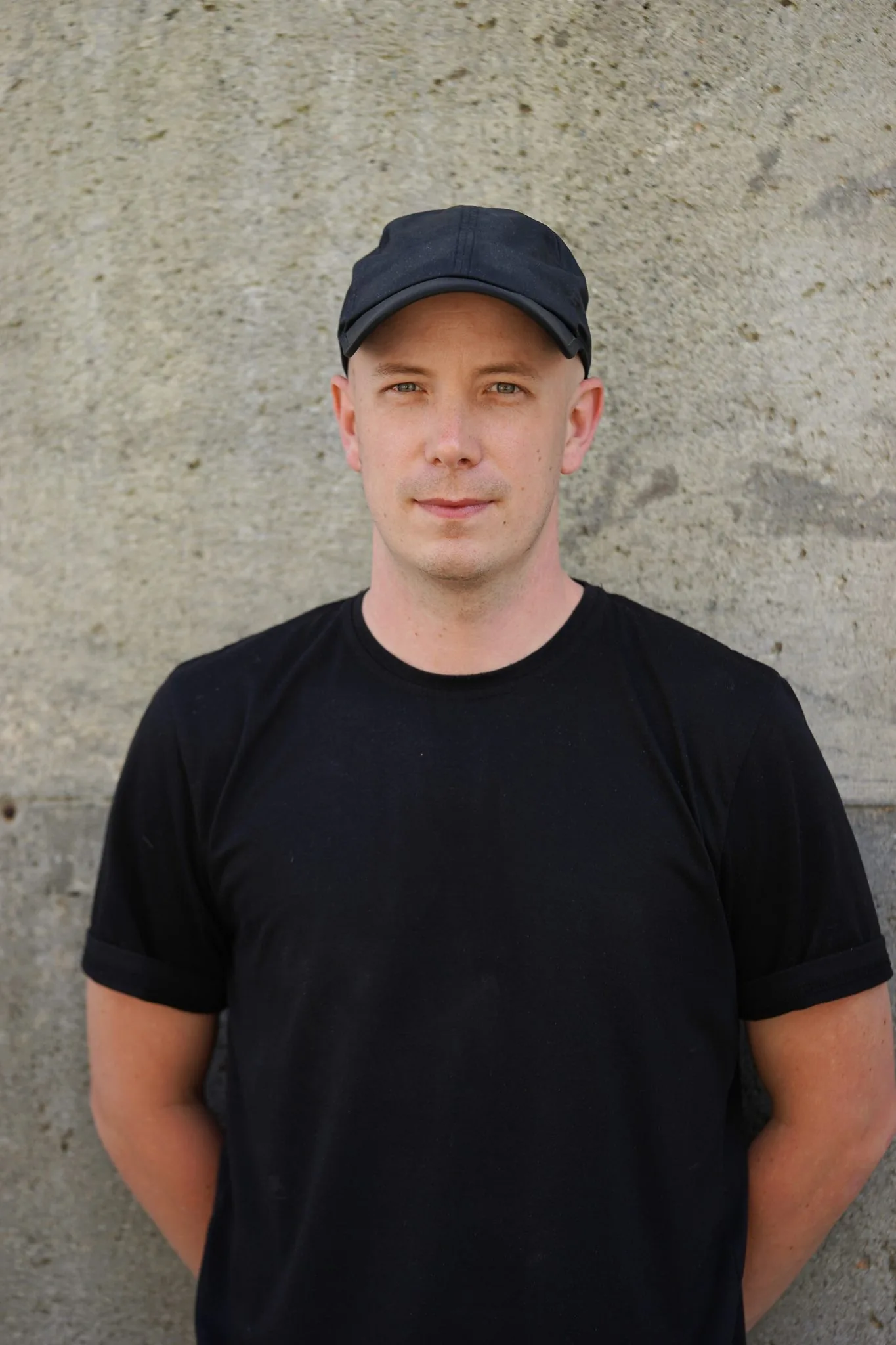 James K, Core Instructor, in a black cap and t-shirt against a concrete wall