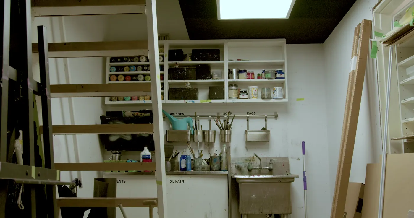 Shelves of shared paints, brushes and materials above the studio wash station