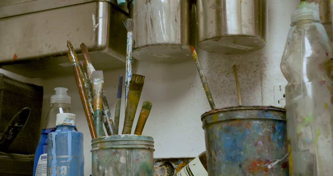 Well-used paintbrushes standing in jars at the studio's paint station