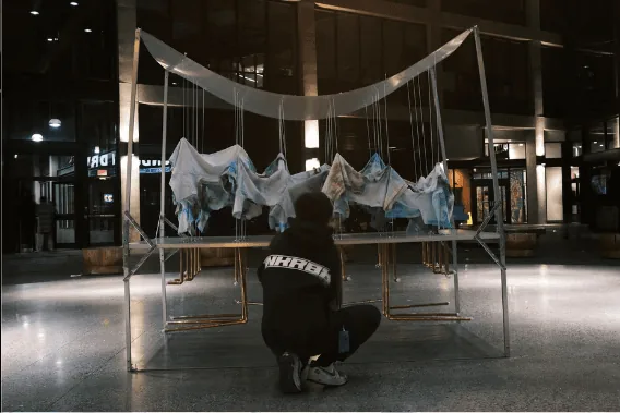Student crouching in front of a suspended fabric sculpture installation displayed at night