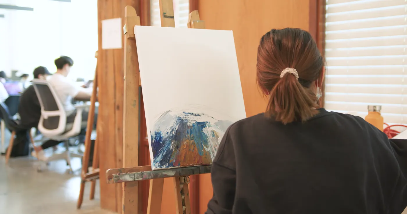 Student blocking in an abstract painting at an easel during a studio session