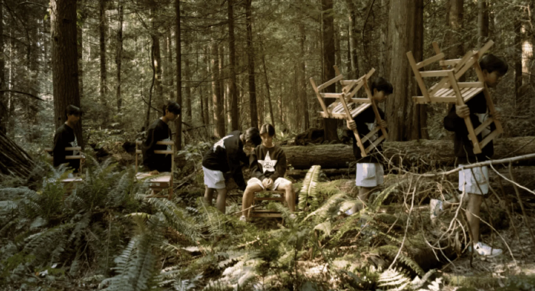Students carrying handmade wooden chairs through a forest for a real-world design project