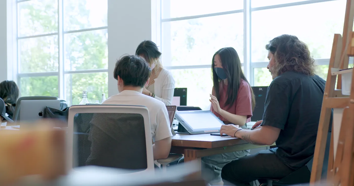Students working side by side on tablets and laptops beside the studio windows