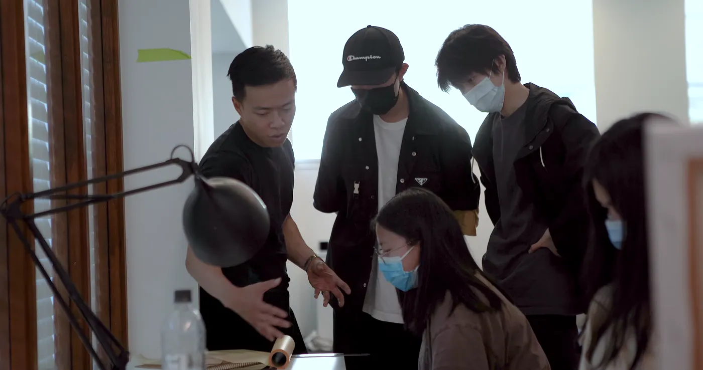 Students gathered around a desk lamp inspecting a group project
