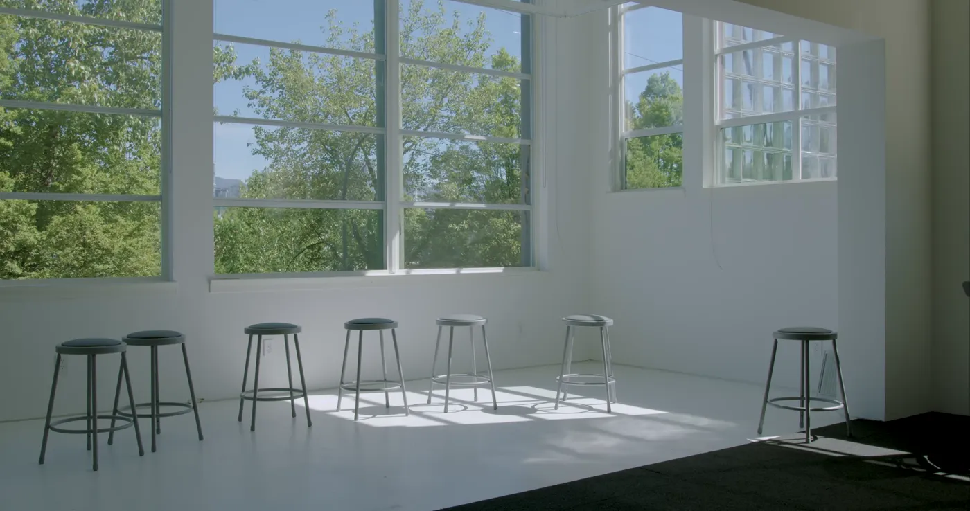 Morning light falling across the empty studio loft and its row of metal stools